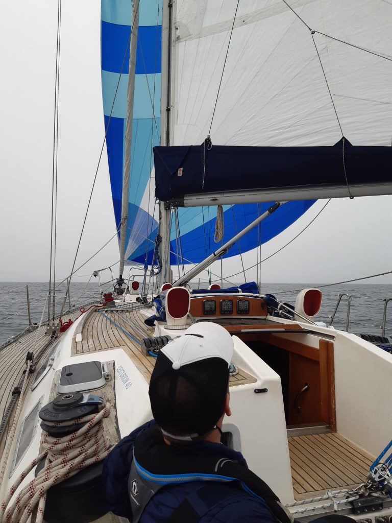 Dark blue and light blue radial asymmetric spinnaker flying, with crew in foreground and grey sea and sky.