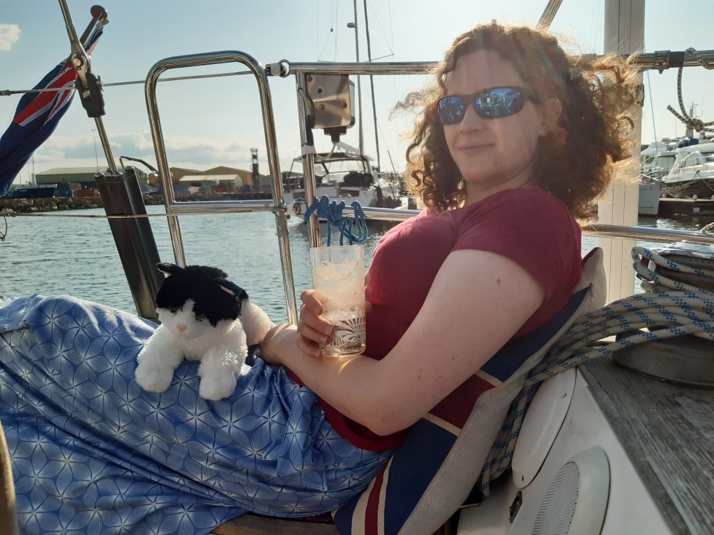 Miranda sitting in the cockpit with Trim on her lap and holding a G&T